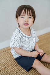Avauma breeze garden baby setup indigo whisper - toddler smiling in white floral t-shirt and navy shorts sitting on rug